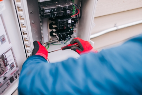 An Energy Technician works on wiring and connections on an electrical breaker box on the exterior of a home